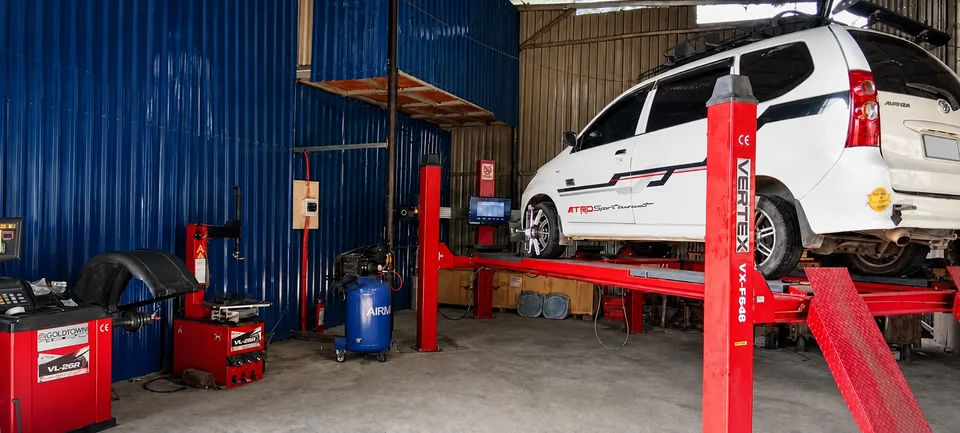 White vehicle on a red lift beside CASAMOTO workshop equipment, with a blank license plate
