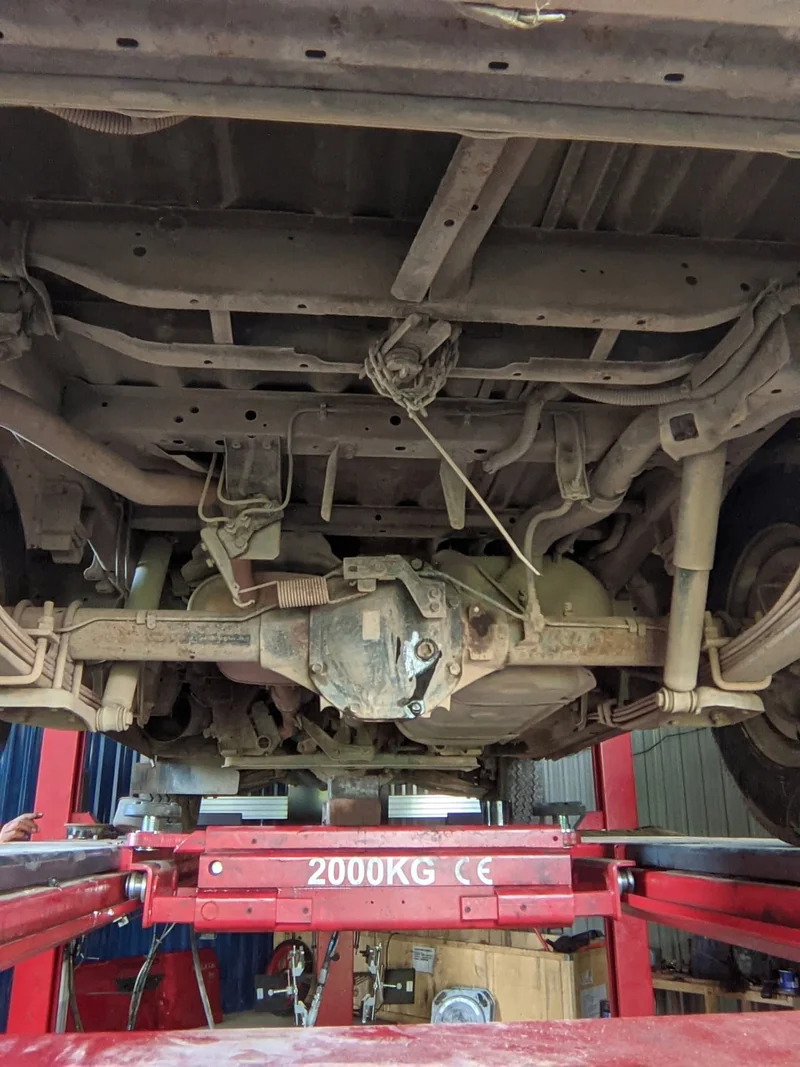 Underside of a vehicle showing the rear axle, suspension and chassis above a red lift